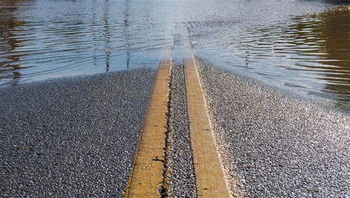 An asphalt road with a double-yellow center line disappearing under floodwater
