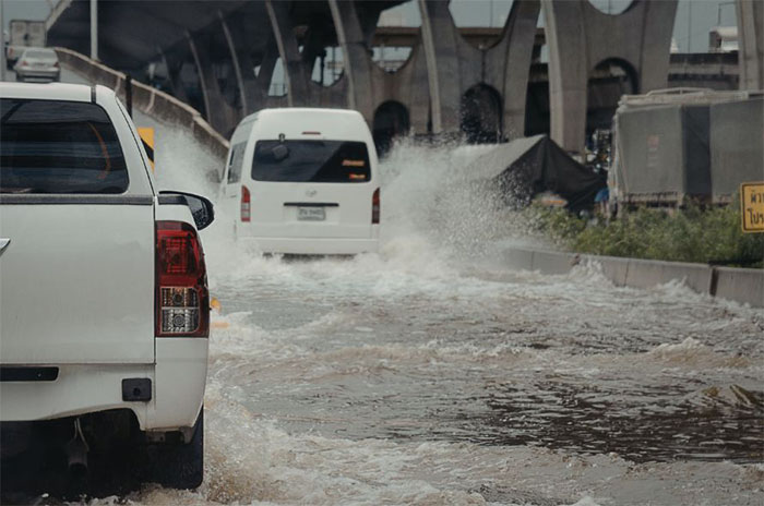Vehicles driving through deep floodwater on a road beneath a bridge